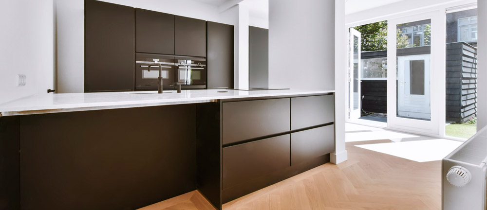 Modern black cabinetry with white quartz countertops and herringbone wood flooring in a bright kitchen – custom design for home renovation.