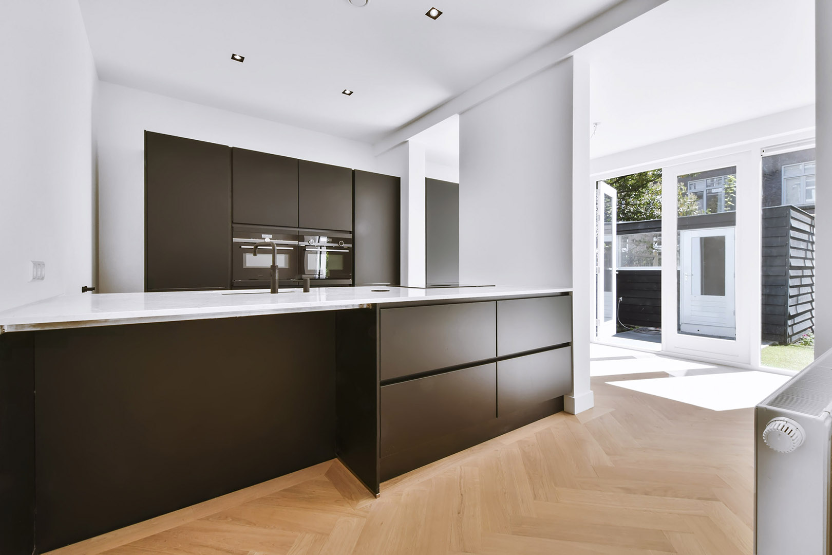 Modern black kitchen cabinets with white countertops and herringbone wood flooring – Corpus Christi home renovation.